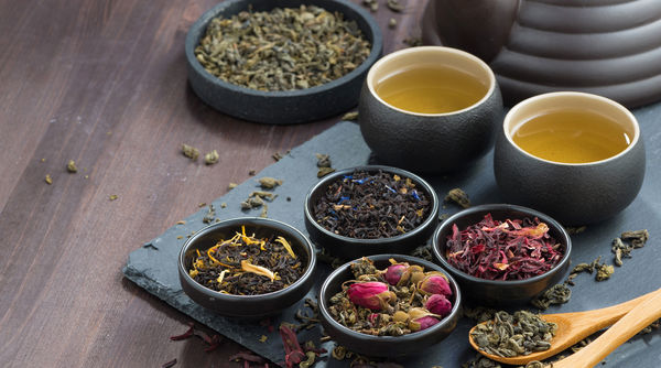 Various types of ground tea in small, black bowls on a black plate