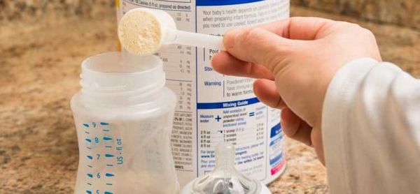 Babyfood in powder form is added to a drinking bottle with a measuring spoon